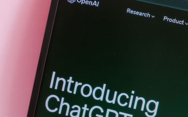 Close-up of a laptop with ChatGPT introduction on screen against a pink background.